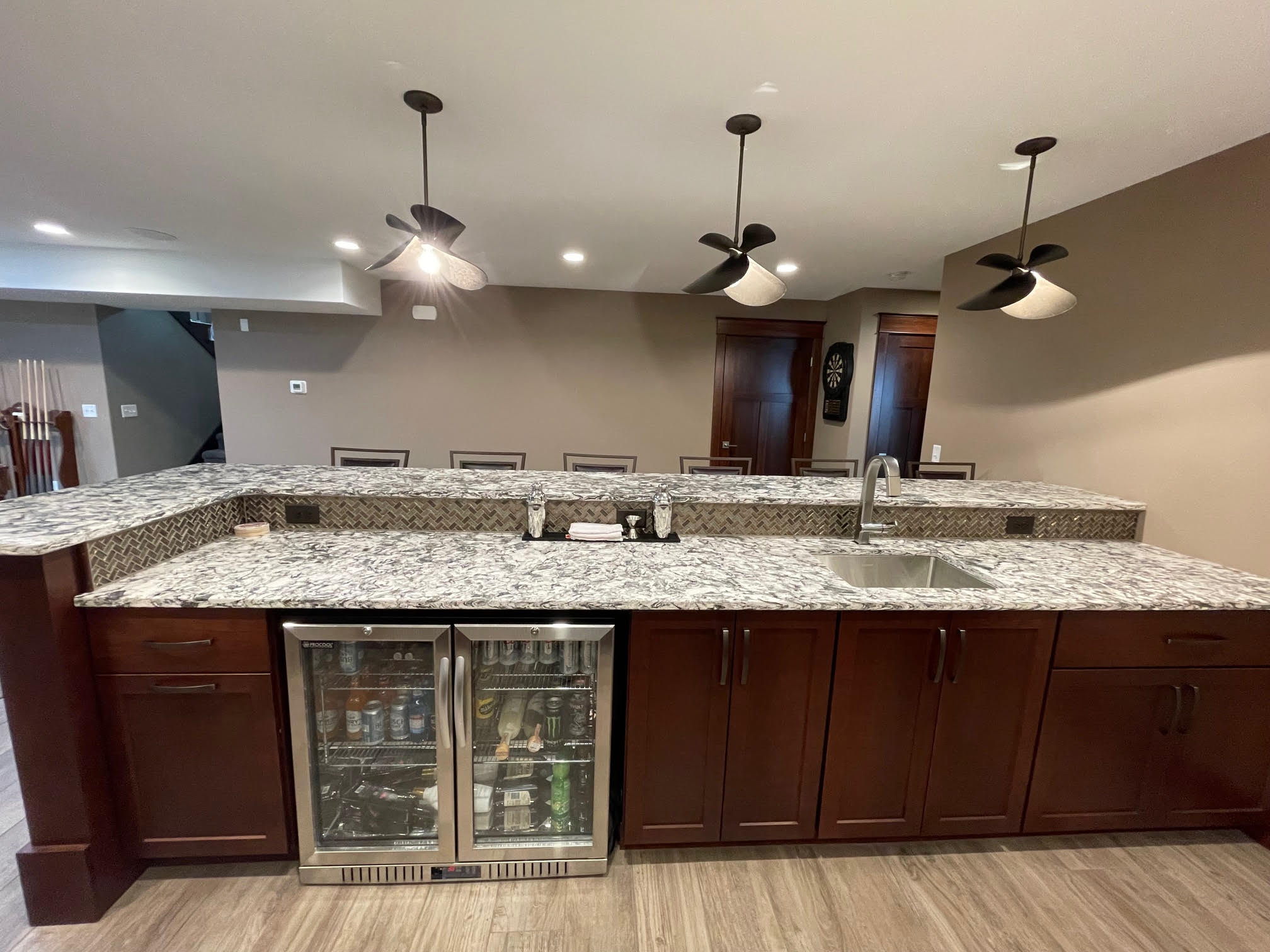 Wet bar in finished basement with gray granite countertops and patterned backsplash